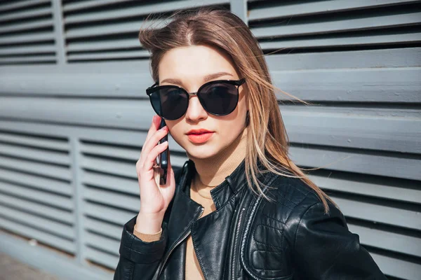 Moda piękny portret ładna kobieta w stylu black rock w okulary za pomocą telefonu komórkowego na szarym tle, w mieście — Zdjęcie stockowe