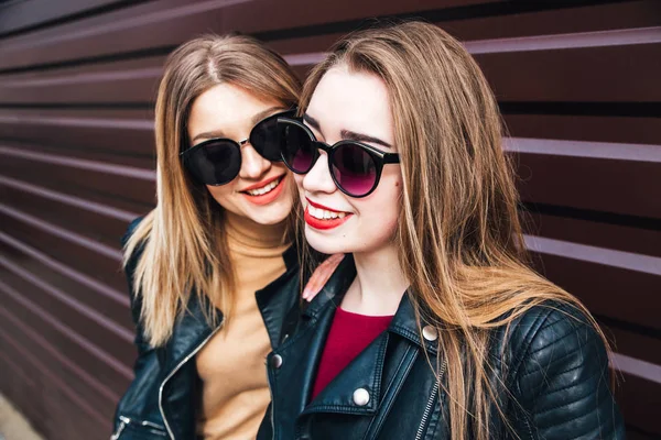 Duas mulheres conversando na cidade.Retrato de estilo de vida ao ar livre de dois melhores amigos meninas hipster vestindo jaqueta de couro elegante e óculos de sol, enlouquecendo e se divertindo muito juntos — Fotografia de Stock