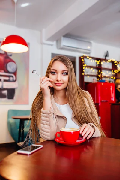 Симпатичная девушка в кафе с улыбающейся кофей.Портрет молодой красивой женщины, пьющей кофе и выглядывающей с улыбкой из кофейни — стоковое фото