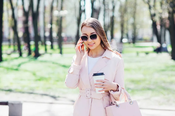 Donna alla moda con telefono e caffè in città. Donna di moda in occhiali da sole e giacca rosa all'aperto — Foto Stock