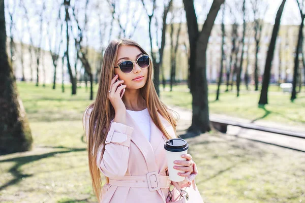 Mujer de moda con teléfono y cofee en la ciudad. Mujer de moda en gafas de sol y chaqueta rosa al aire libre — Foto de Stock