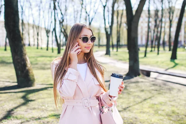 Mujer de moda con teléfono y cofee en la ciudad. Mujer de moda en gafas de sol y chaqueta rosa al aire libre — Foto de Stock