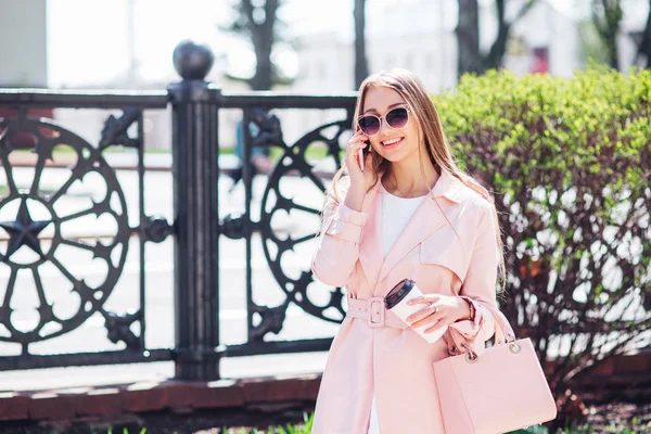 Mujer de clase alta. Mujer de moda enviando mensajes al aire libre. Mujer de moda en gafas de sol y chaqueta rosa con café — Foto de Stock