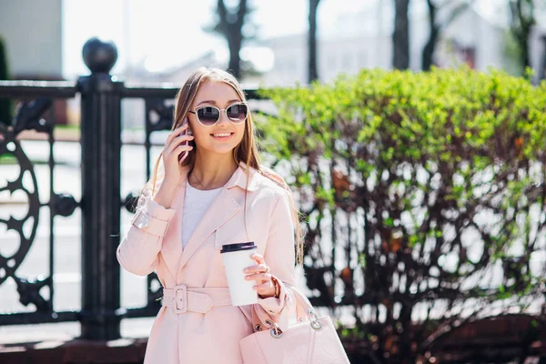 Mujer de clase alta. Mujer de moda enviando mensajes al aire libre. Mujer de moda en gafas de sol y chaqueta rosa con café — Foto de Stock