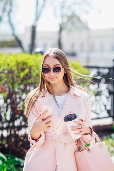 Mujer de clase alta. Mujer de moda enviando mensajes al aire libre. Mujer de moda en gafas de sol y chaqueta rosa con café — Foto de Stock