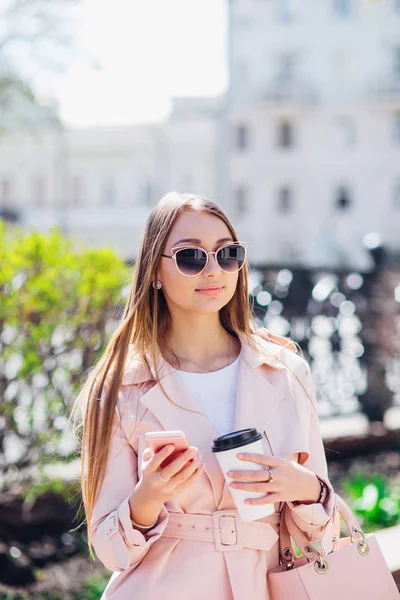 Mujer de clase alta. Mujer de moda enviando mensajes al aire libre. Mujer de moda en gafas de sol y chaqueta rosa con café — Foto de Stock