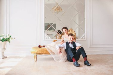 Gelin Damat gibi beyaz studio iç içeride kanepe evde oturan siyah takım elbiseli ve güzel bir elbise. Moda düğün tarzı .