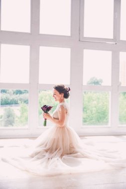 Ararken bir lüks elbiseli güzel sevimli gelin. Portre, mutlu gelin oturan gelinlik bir stüdyoda. Çiçekli genç çekici gelin