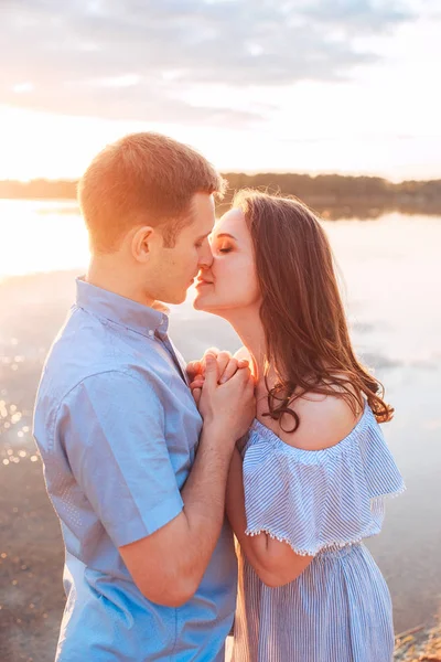 Jonge mooie paar verliefd verblijft en zoenen op het strand op zonsondergang. zachte zonnige kleuren. — Stockfoto