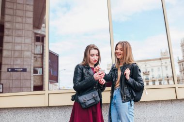 İki mutlu kadın arkadaşlar açık havada şehirde bir akıllı telefon olarak sosyal medya paylaşımı. Cep telefonu konuşma ile iki genç kadın