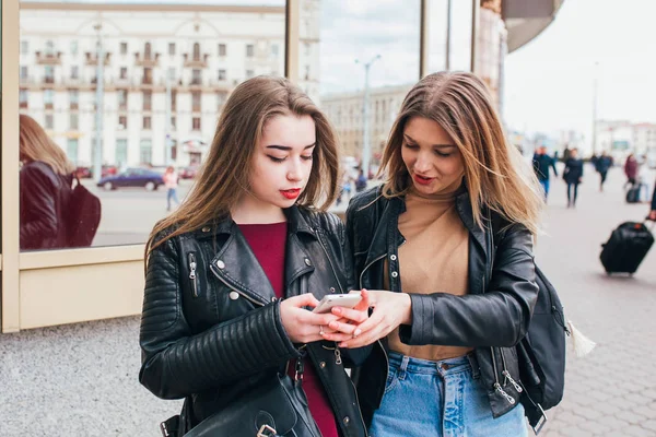 Two happy women friends sharing social media in a smart phone outdoors in city . Two Young Women with Mobile Phone talking
