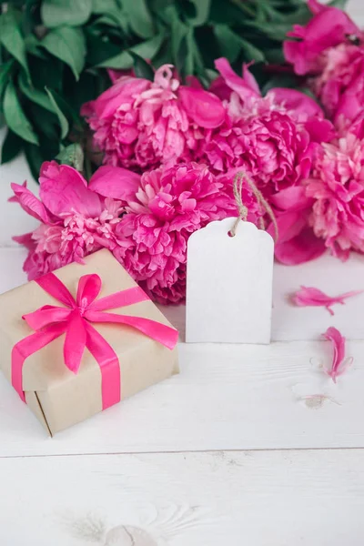 Roze pioenrozen bloemen en lege tag op leeftijd houten achtergrond. Bovenaanzicht met kopie ruimte. Moeders of Womens dag — Stockfoto