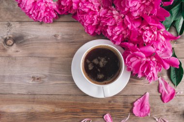 Bir fincan kahve, pembe peonies desen ahşap arka plan üzerinde. Günaydın. Kadın ya da anneler günü arka plan. Üstten Görünüm