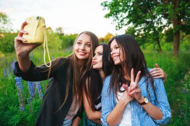 Üç hipsters kızlar sarışın ve esmer açık portresi polaroid fotoğraf makinesi ve gülümseyen alarak. Parkta birlikte eğlenmek kızlar.