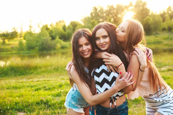 Três mulheres abraçando umas às outras ao ar livre e rindo ao pôr do sol . — Fotografia de Stock