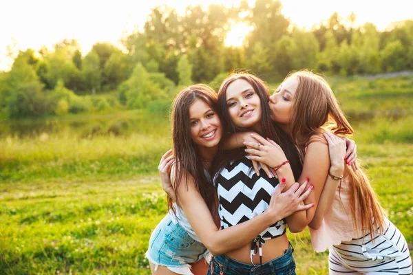 Drie vrouwen buitenshuis omhelzen elkaar en lachen op zonsondergang. — Stockfoto