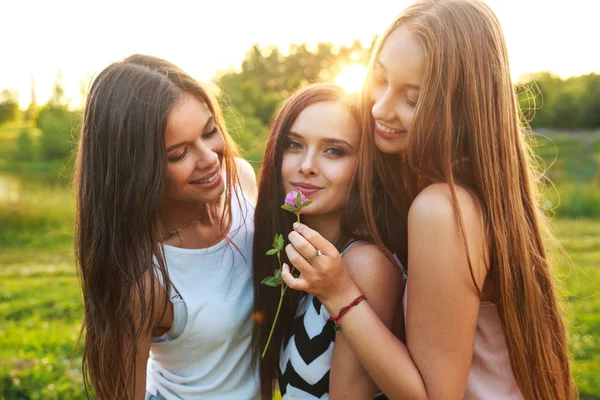 Drie vrouwen buitenshuis omhelzen elkaar en lachen op zonsondergang. — Stockfoto