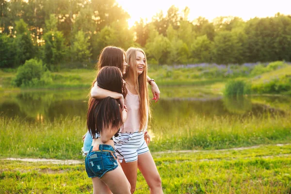 Drei schöne Mädchen, die bei Sonnenuntergang im Park spazieren gehen und lachen. Freundschaftskonzept. — Stockfoto