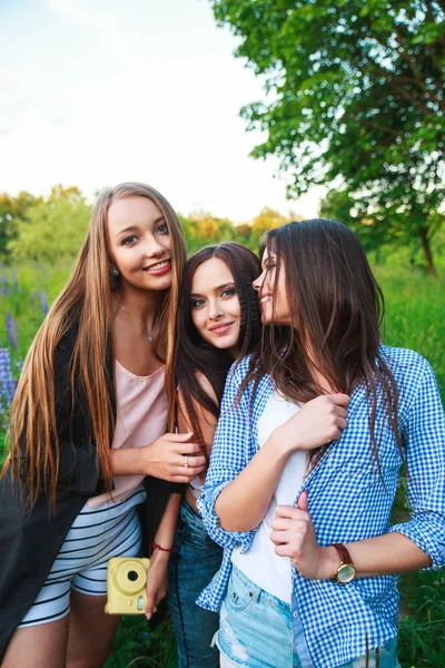 Három hippik lányok blonde- és brunette véve önarckép a polaroid fényképezőgép és mosolyogva szabadtéri. A lányok érzik magukat együtt a park. — Stock Fotó