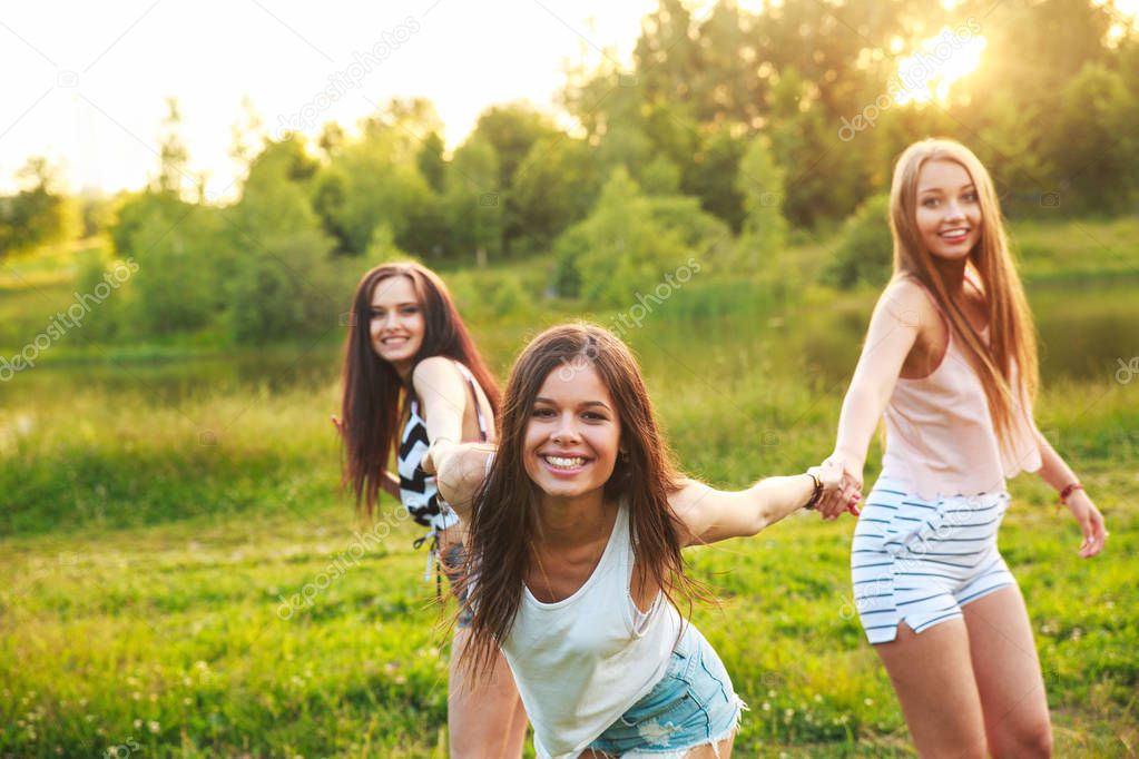 three beautiful girls walking and laughing on sunset in the park. Friendship concept.