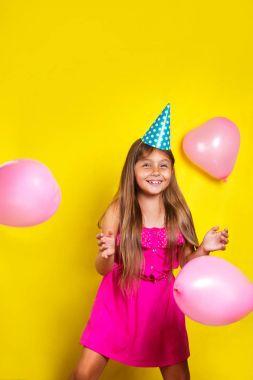 Stüdyo portre onun doğum gününde bir parti şapka giymiş küçük bir kız. Renkli balonlar ile mutlu kız