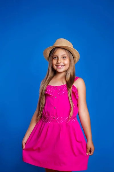 Retrato de niña linda en vestido rosa y sombrero sobre fondo azul. Vacaciones de verano y concepto de viaje — Foto de Stock