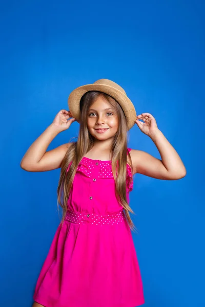 Retrato de niña linda en vestido rosa y sombrero sobre fondo azul. Vacaciones de verano y concepto de viaje — Foto de Stock