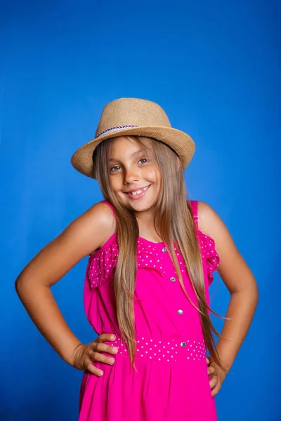 年轻可爱的女孩，在粉红色的裙子和帽子在蓝色背景上的肖像。暑假和旅行概念 — 图库照片