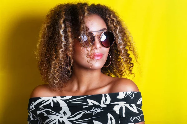 Retrato dentro de casa de uma jovem afro-americana de óculos de sol. Fundo amarelo. Estilo de vida. Vestuário casual — Fotografia de Stock