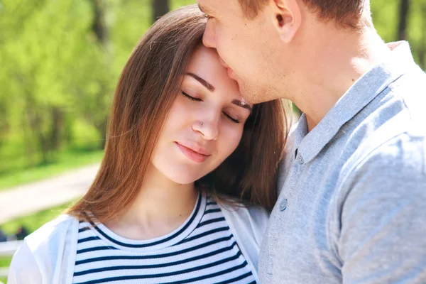 Красивий чоловік і його красива вагітна дружина обіймаються і посміхаються, стоячи в парку — стокове фото