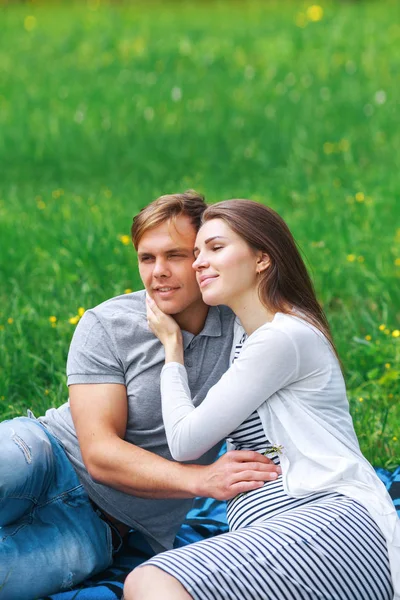 Glückliche schwangere Frau mit ihrem Mann, der sich im Park umarmt und lächelt — Stockfoto