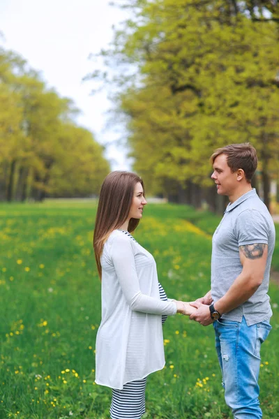 Gravid kvinna med man promenader och håller händer i parken — Stockfoto