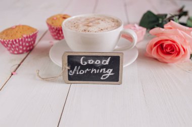 Kahve kupa ile kek, gül ve Günaydın yukarıdan, sıcak ve lezzetli bir kahvaltı beyaz rustik masada notları