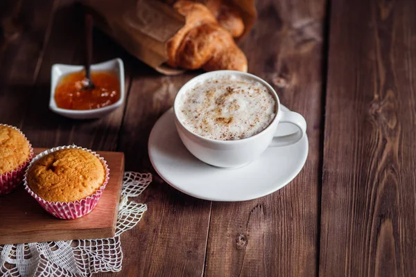 Kahve Kupası ve kahve çekirdekleri, kruvasan, kek, kahverengi ahşap masa üzerinde portakal reçeli