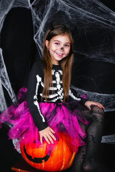 Niedliches kleines Mädchen sitzt auf dem Kürbis auf schwarzem Hintergrund mit einem Spinnennetz — Stockfoto