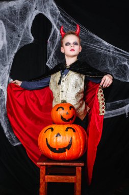 Cadılar Bayramı da genç bir çocuk şeytan kostümü ile eğleniyor bir örümcek ağı ile siyah arka plan üzerine kabaklar