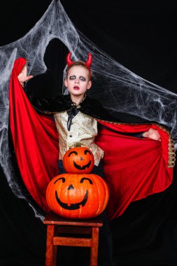 Cadılar Bayramı da genç bir çocuk şeytan kostümü ile eğleniyor kabaklar