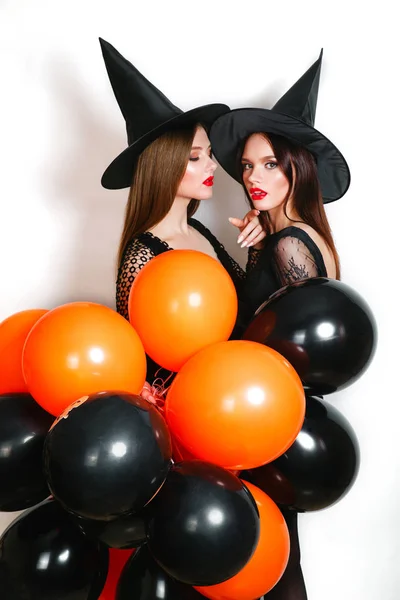 Twee gelukkige sexy vrouwen in het zwart heks halloween kostuums met oranje en zwarte ballon op partij op witte achtergrond — Stockfoto