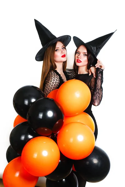 Twee gelukkige sexy vrouwen in het zwart heks halloween kostuums met oranje en zwarte ballon op partij op witte achtergrond — Stockfoto