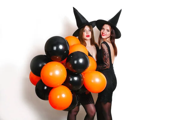 Två glada sexiga kvinnor i svart häxa halloween kostymer med orange och svart ballong part över vit bakgrund — Stockfoto