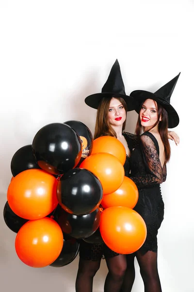 Twee gelukkige sexy vrouwen in het zwart heks halloween kostuums met oranje en zwarte ballon op partij op witte achtergrond — Stockfoto