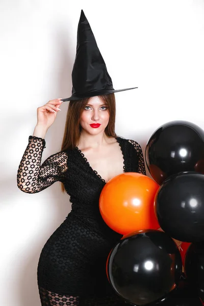 Portret van mooie jonge vrouw in zwarte heks halloween kostuum met oranje en zwarte ballonnen op witte achtergrond — Stockfoto