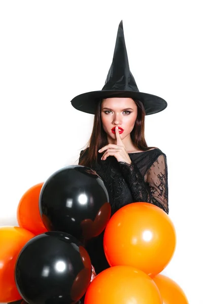 Portret van mooie jonge vrouw in zwarte heks halloween kostuum met oranje en zwarte ballonnen op witte achtergrond — Stockfoto
