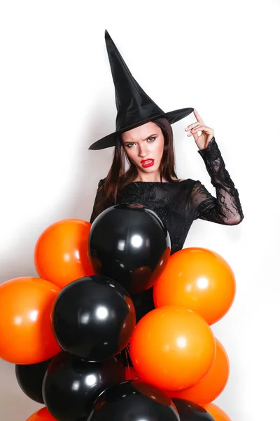 Portret van mooie jonge vrouw in zwarte heks halloween kostuum met oranje en zwarte ballonnen op witte achtergrond — Stockfoto