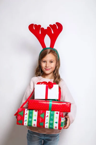 Счастливая маленькая улыбающаяся девочка с подарком на Рождество. Улыбающаяся смешная девушка в оленьих рогах в студии . — стоковое фото