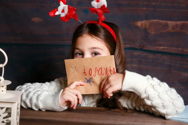 Niño escribe carta a Santa Claus. Chica divertida en Santa sombrero escribe carta a Santa —  Fotos de Stock