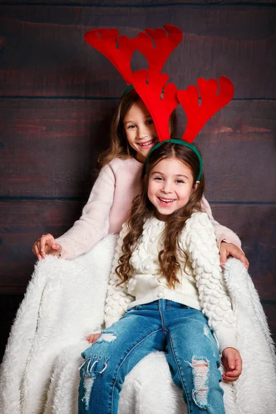 Две счастливые маленькие улыбающиеся девочки обнимаются. Рождественская концепция. Улыбающиеся смешные сестры в оленьих рогах в студии . — стоковое фото