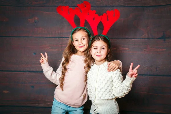 Dos niñas sonrientes felices divirtiéndose concepto .Christmas. Sonrientes hermanas divertidas en cuernos de ciervo sobre fondo de madera — Foto de Stock
