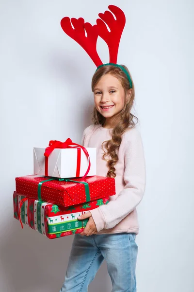 Feliz Navidad y feliz año nuevo .happy niña sonriente con cajas de regalo de Navidad.. Sonriente niño divertido en cuernos de ciervo —  Fotos de Stock