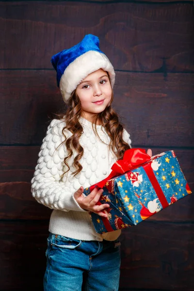 Feliz niña sonriente con regalo de Navidad box.Christmas concepto. Sonriente chica bastante divertida en Santa sombrero sobre fondo de madera . —  Fotos de Stock